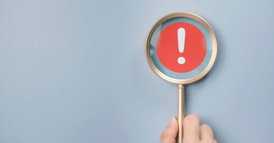 Red alert warning in a magnifying glass in front of a blue background.