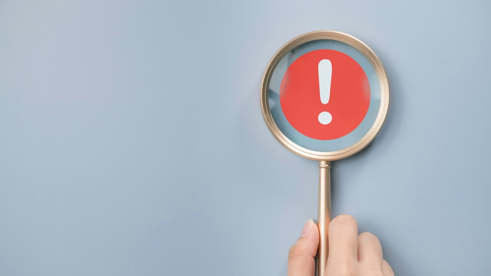 Red alert warning in a magnifying glass in front of a blue background.