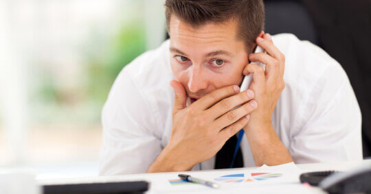 A businessman in a white shirt and tie making a private phone call in his office