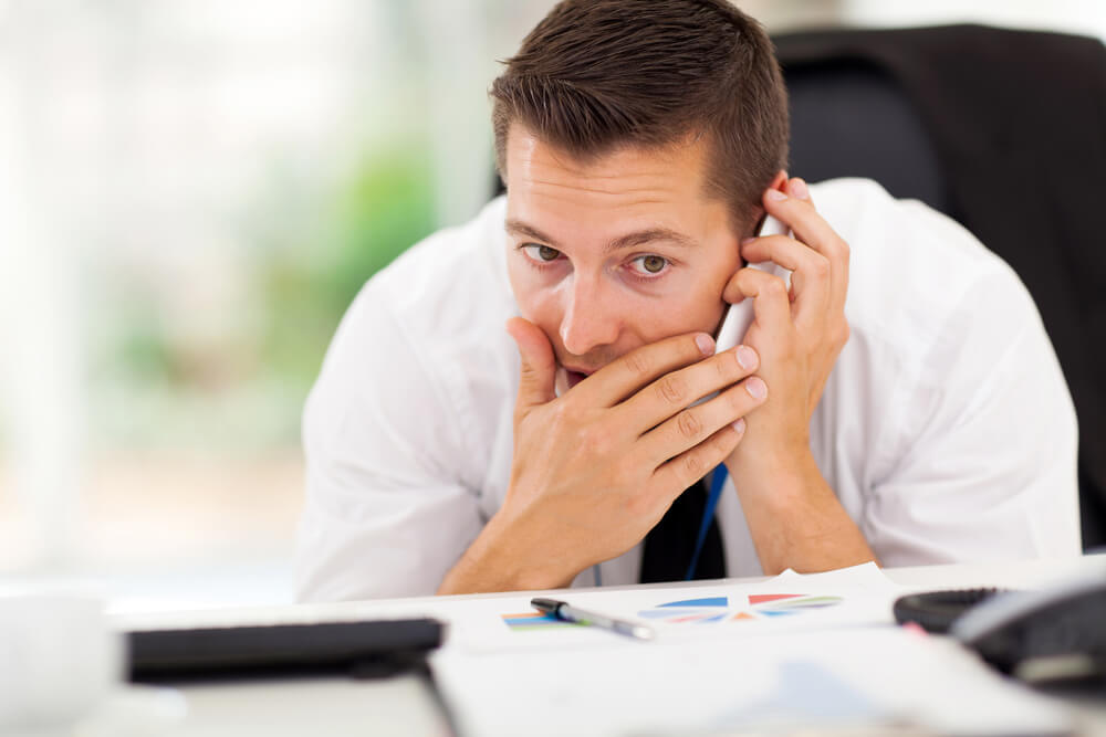 A businessman in a white shirt and tie making a private phone call in his office