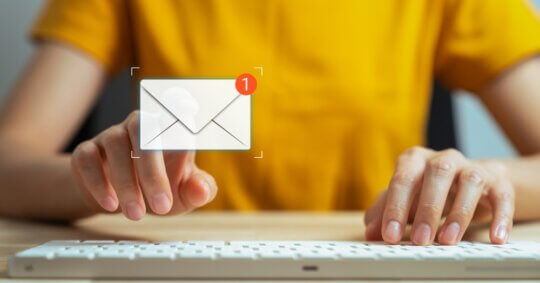 A person typing a message on a keyboard and tapping a digital screen to find an email address among new notifications.
