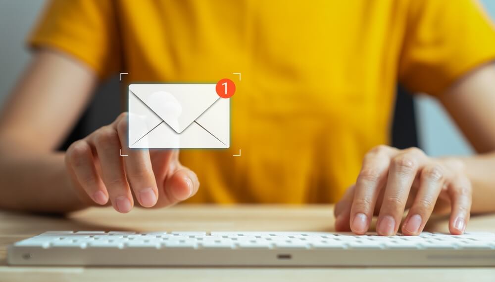 A person typing a message on a keyboard and tapping a digital screen to find an email address among new notifications.