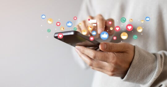 Adult man holding a phone and using a social media app to reply to messages and react with emojis.