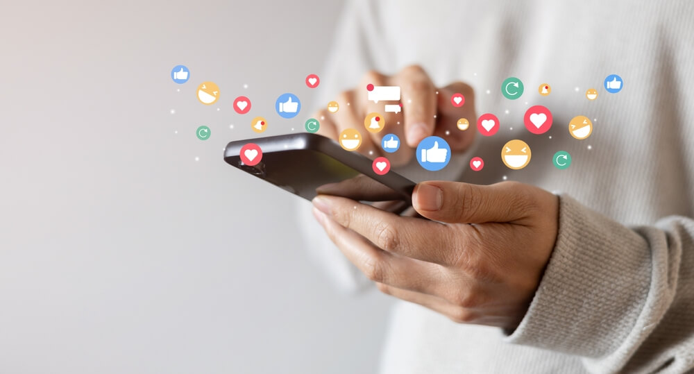 Adult man holding a phone and using a social media app to reply to messages and react with emojis.