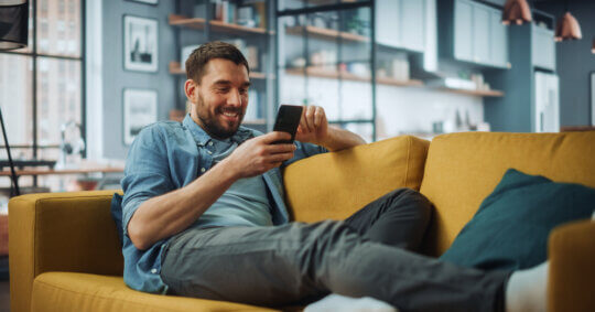 Close-up of a man on a sofa taking time to search people on WhatsApp with their smartphone.