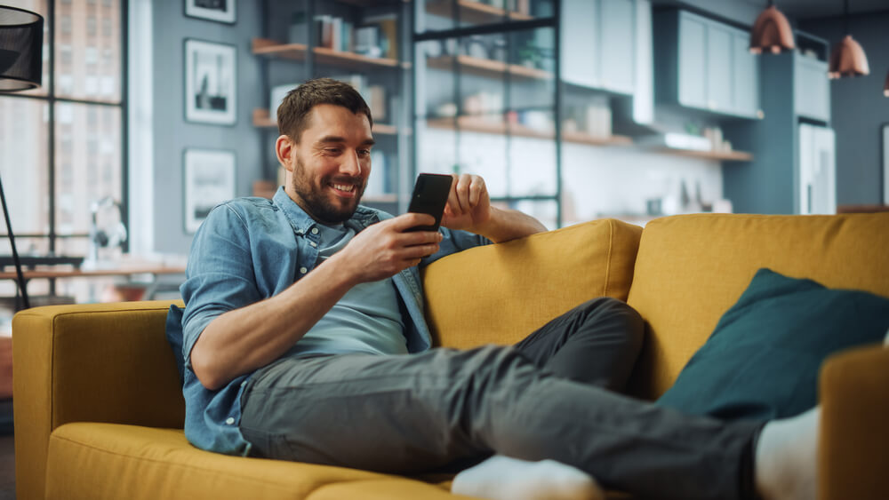Close-up of a man on a sofa taking time to search people on WhatsApp with their smartphone.