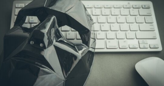 Close-up photo of a black mask resting on a keyboard implying the importance of catfish people search and online identity verification.