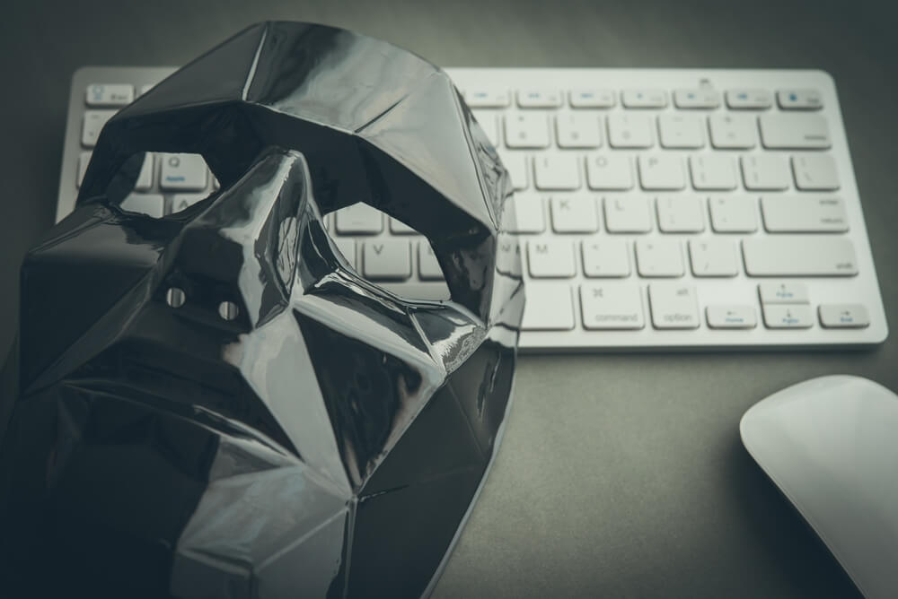 Close-up photo of a black mask resting on a keyboard implying the importance of catfish people search and online identity verification.