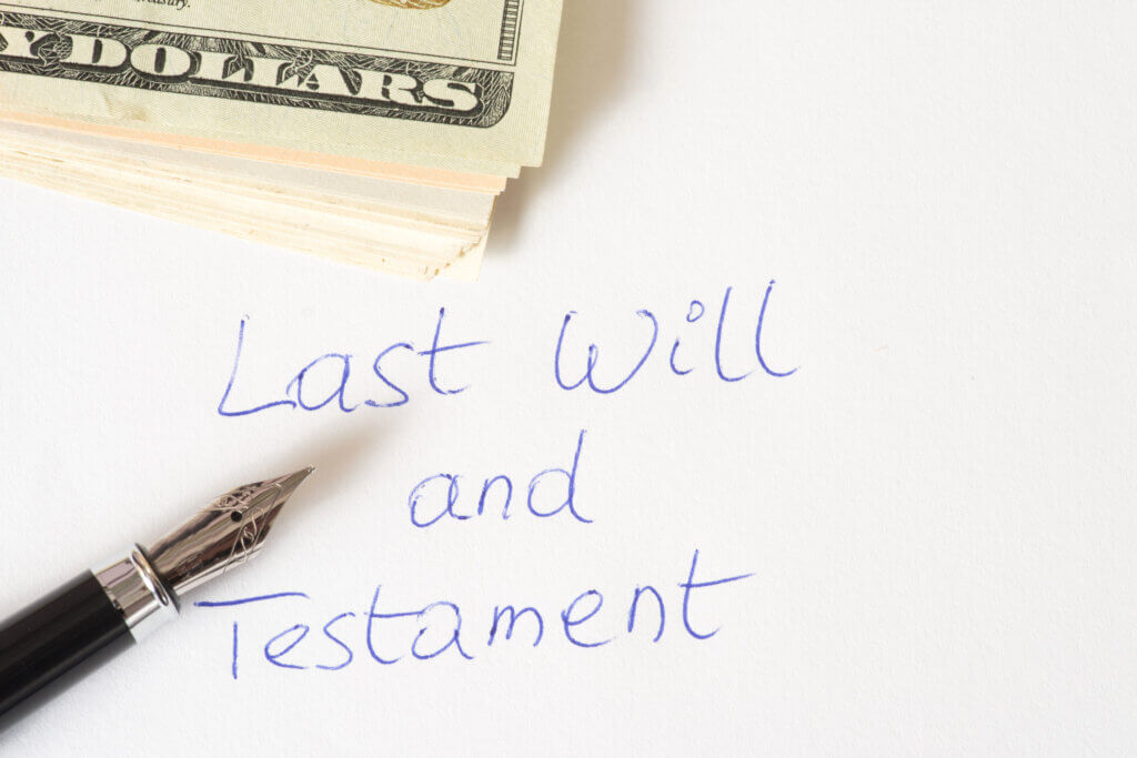 A pen atop a last will and testament and dollar bills.