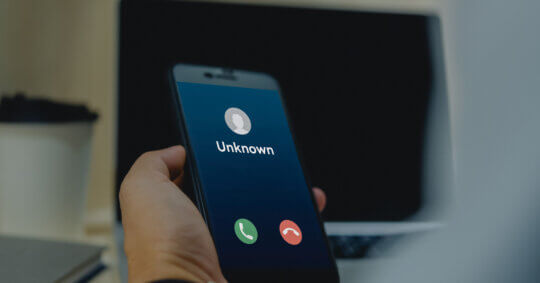 Close up of a phone screen with an incoming call labeled “unknown” through built-in service or third-party phone number scammer lookup tool.